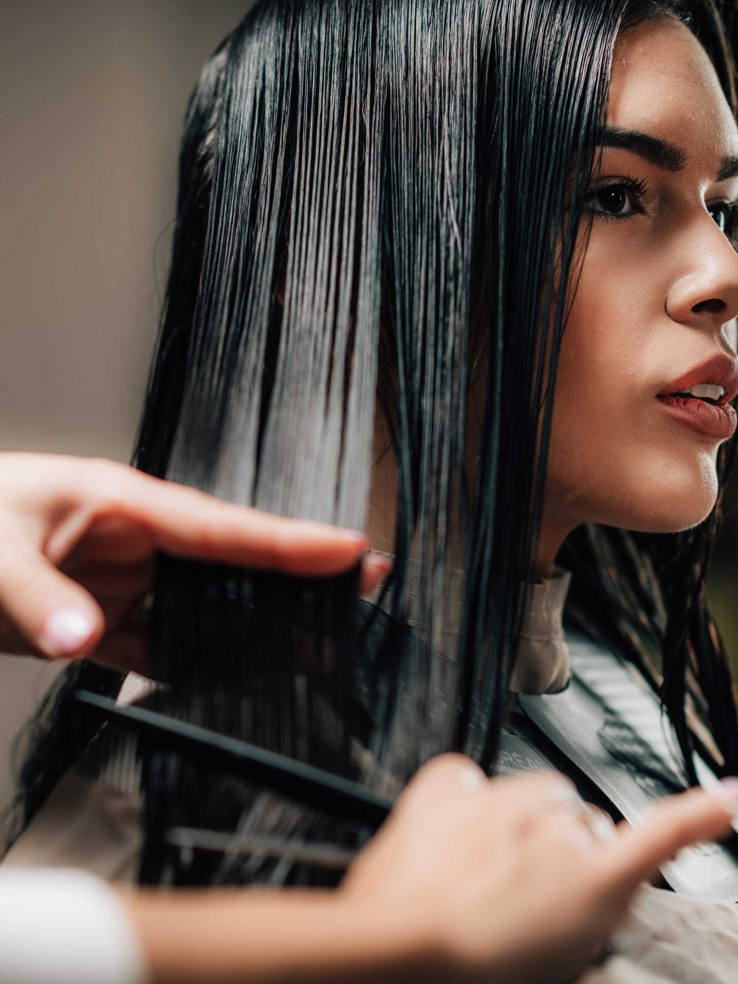 Woman getting a professional haircut with long, straight, wet hair being trimmed by a stylist.