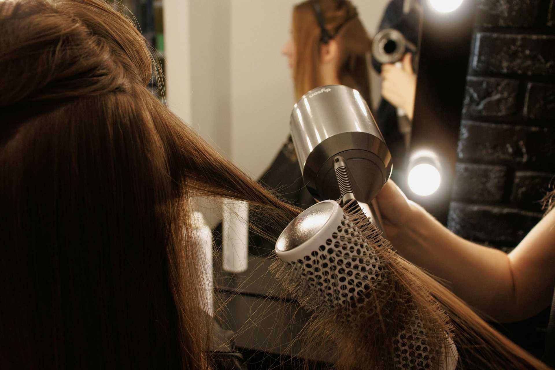 A hairdresser blow-drying and styling a woman's hair in a salon.