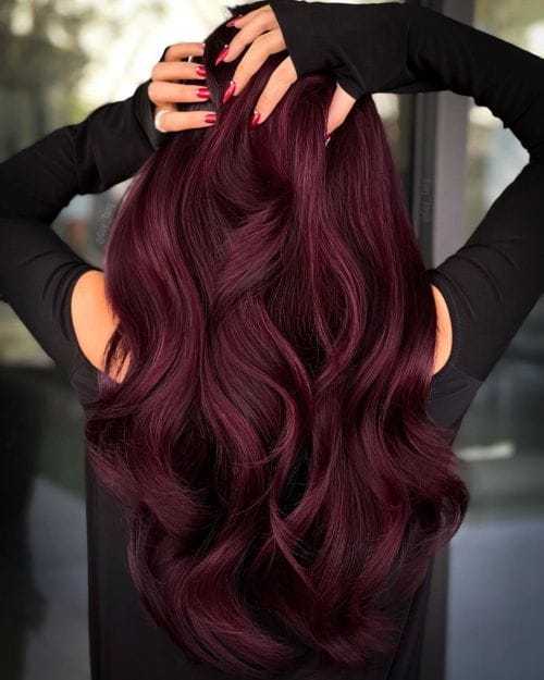 A person with long, wavy, dark burgundy hair, styled and flowing down their back.